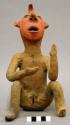 Ceramic figurine, female human seated, red & black painted face & genitals.