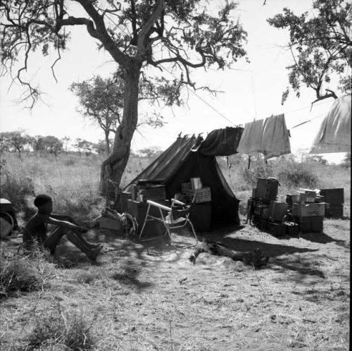 Boy sitting, with an expedition tent and sound equipment near him