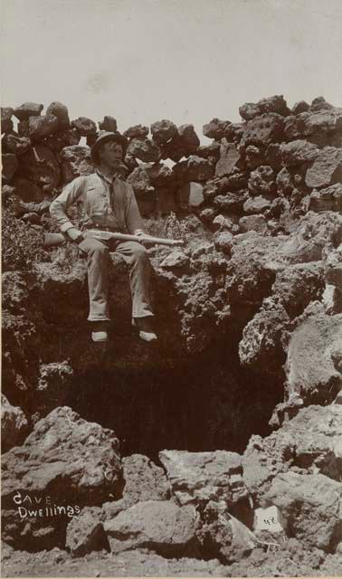 Man with a rifle seated among ruins