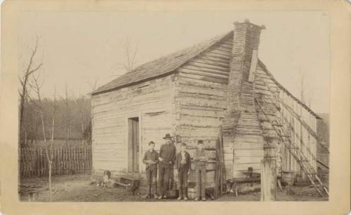 Man and boys standing in front of a cabin