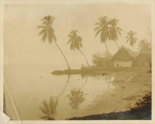 People, thatched-roof huts, and a canoe on the shore of a body of water