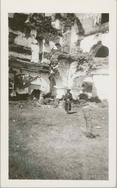 Woman standing center frame, ruined building in background