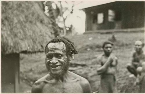 Three men standing, with buildings in background