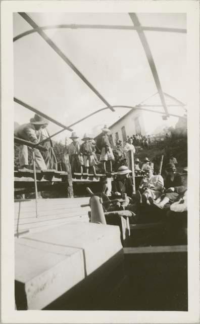 View inside docked boat, two men and two women sitting, dock busy