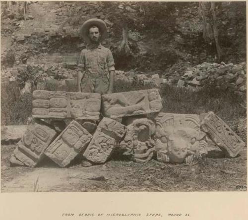 Man standing behind sculptures from debris of hieroglyphic steps, Mound 26