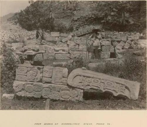 Man standing among sculptures from debris of hieroglyphic steps, Mound 26