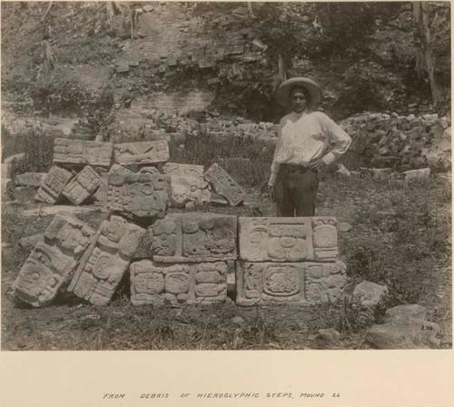 Man standing behind sculptures from debris of hieroglyphic steps, Mound 26