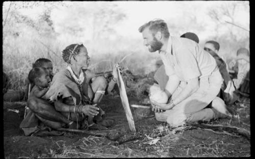 Di!ai preparing wood for a fire, and Daniel Blitz watching her; Di!ai's child is crying