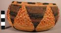Small round coiled basket, brown woven pattern, feather ornament.
