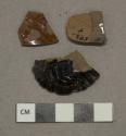 Dark brown lead glazed redware vessel body fragment, grayish red paste, 1 with fluted decoration