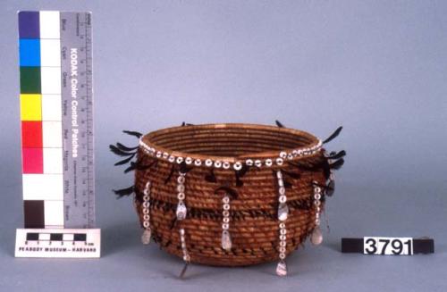 Small coiled circular basket, feather and shell ornament.