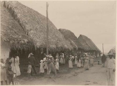 People on road in front of thatch-roofed buildings