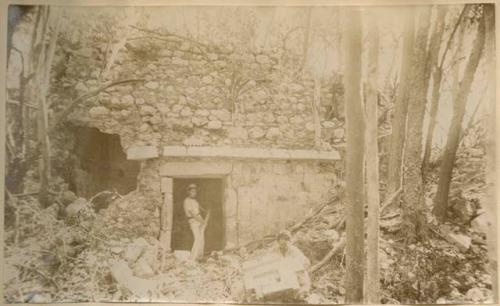 Two men near structure covered in vegetation