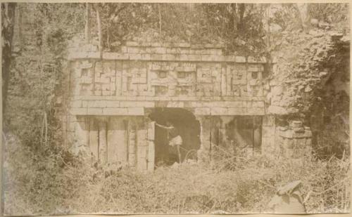 Man standing in structure covered in vegetation, possibly in Xkichmook