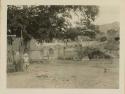 Person standing next to fence, dog, and building in background