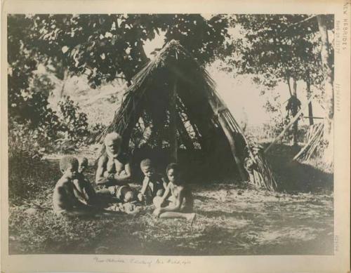 Man and four boys sitting in front of a hut