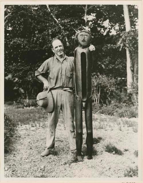 Man standing next to wooden anthropomorphic drum