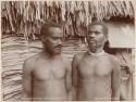 Two men standing in front of thatched structure