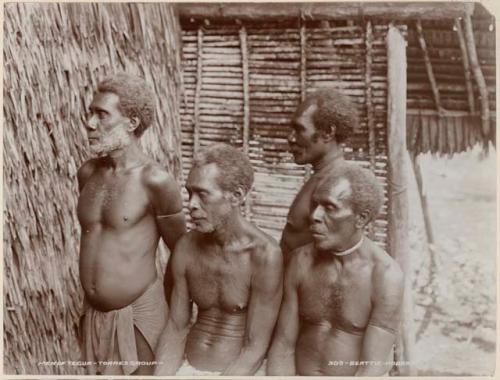 Four men of Tegue standing in front of a thatched structure