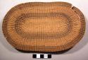 Small flat basketry mat, elliptical, with yellow and brown grasses