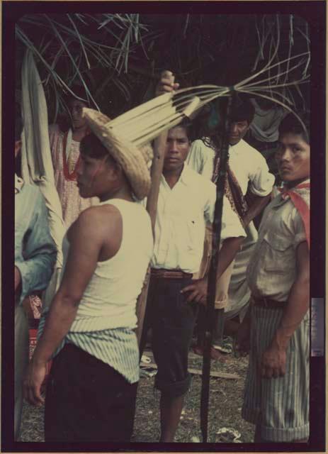 Ngobe-Bugle crowd under thatch-roofed canopy, man in front has film reel on headdress