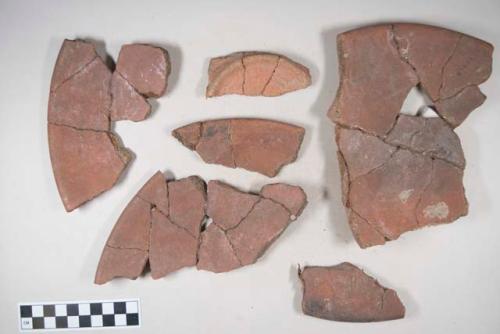 Earthenware vessel sherds; red paint interior; possible plate with ring foot base. Some sherd show charring.