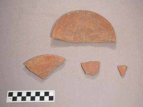 Earthenware vessel body and rim sherds. Red paint decoration interior and exterior. Plate-like shape. Possible pot cover.