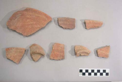 Earthenware vessel rim, body, and base sherds with red paint decoration. Paste is very friable. Base sherds are foot ring fragments.