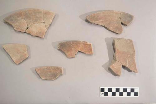 Earthenware vessel body, base, and rim sherds with red paint decoration. Some sherds show charring. Base fragments are foot ring sherds