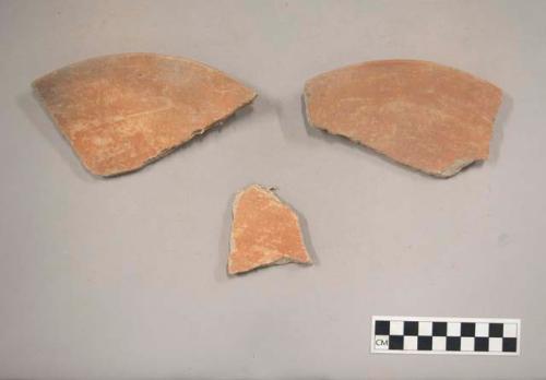 Earthenware vessel rim and body sherds with red paint interior and exterior. Charring.