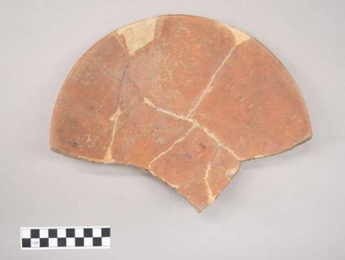 Earthenware plate-like vessel sherds mended with glue and stained plaster of paris replacement of voids forming a partially complete plate with ring-footed base. Red painted interior and exterior (except plaster sherds)