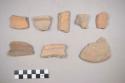 Earthenware vessel rim and body sherds. Most with red paint interior and exterior. One paddle decorated in horizontal lines.