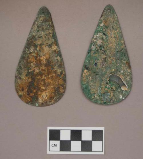 Metal, copper alloy ornaments, flat, tear drop shaped, perforated at narrow end, one with iron and mica adhered to it, one with bone, shells, and charcoal adhered to it