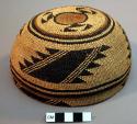 Twined basketry cap: brown and black geometric decoration. Diam: approx.17cm