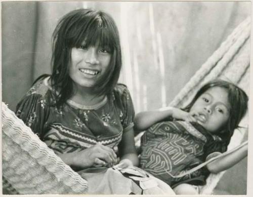 Two girls learning to sew on hammock