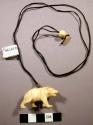 Bone or ivory carving of a bear on a black string with two beads attached.