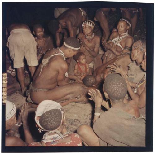 Medicine man leaning over a circle of women and children clapping at a night dance