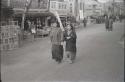 Two women walking down street, with storefronts in background