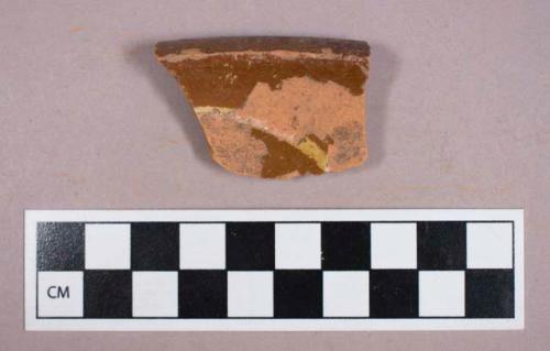 Ceramic, earthenware, brown glazed redware rim sherd with yellow slip decoration