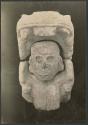 Carved stone human head in mouth of serpent