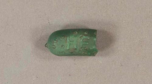 Molded green plastic fragment, with embossed letters "HEI..."; research shows that it is part of a Heinz pickle pin