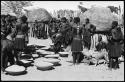 Group of people working with baskets of grain, with dogs next to them