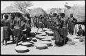 Group of people working with baskets of grain, with dogs next to them