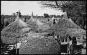 People standing next to large baskets and thatched roofs