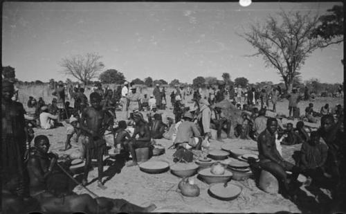 Group of people standing and sitting, with baskets of grain on the ground near them