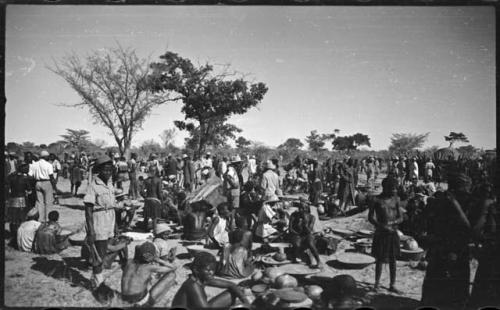 Group of people sitting and standing, with baskets of grain on the ground near them