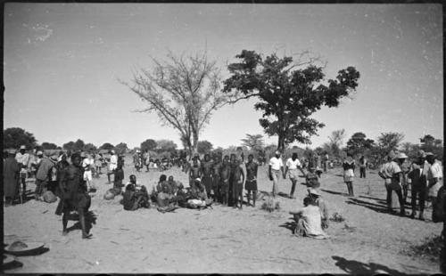 Group of people sitting and standing, with baskets of grain on the ground near them