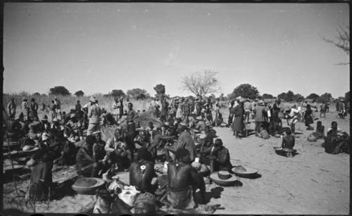 Group of people sitting and standing, with baskets of grain on the ground near them