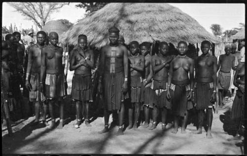 Group of women standing in a line, with thatched roof in background