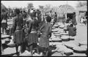 Group of people sitting and standing next to baskets of grain on ground